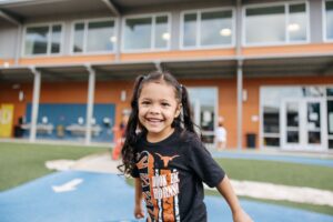 A student with a University of Texas t-shirt on smiling on the playground