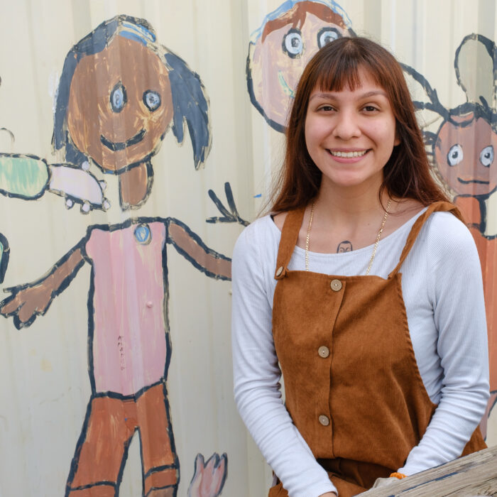 Mariah sits beside a self-portrait her older sister, Andrea, painted in kindergarten. Andrea was a member of UT Elementary’s first kindergarten class.
