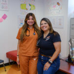 UT Austin Nursing student Daniela Mora in her burnt orange scrubs stands with UT Elementary School Nurse Rachel Ibarra